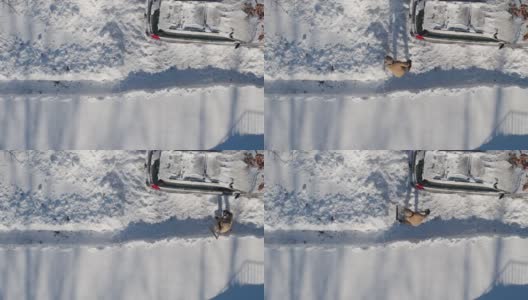 一名成年男子在一场冬季降雪后用铲子清理车道上的积雪。鸟瞰无人机正上方的慢动作视频。高清在线视频素材下载