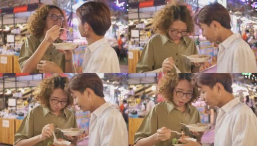 亚洲男性朋友在夜市吃他们买的食物和拍照。高清在线视频素材下载