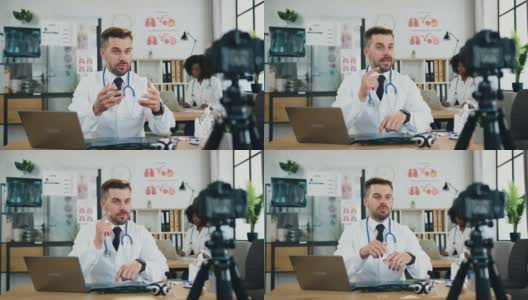 可爱、自信、聪明、合格的大胡子医生坐在他的工作地点的医疗办公室里，为互联网观众录制视频高清在线视频素材下载