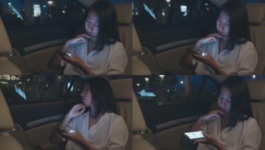 亚洲女商人穿着时尚的办公室服装工作到很晚，在城市现代城市的汽车后座上使用智能手机。高清在线视频素材下载