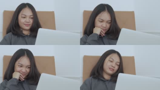 4k, Portrait，一个可爱的亚洲少女。穿着灰色衬衫坐在椅子上，带着笔记本电脑在卧室里开心地上网学习高清在线视频素材下载