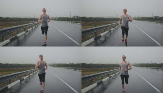 亚洲体育三项全能运动员在下雨时在高速公路上跑马拉松，正面视图。体格健壮的男人沿着公路跑步做有氧运动高清在线视频素材下载
