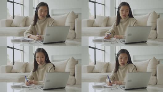 一位亚洲女性戴着耳机看着笔记本电脑屏幕，与对话者交流。韩国女商人戴着耳机视频呼叫客服高清在线视频素材下载