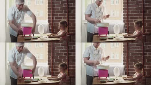 一个男厨师在一个特殊的机器上为一个可爱的小女孩制作棉花糖。高清在线视频素材下载
