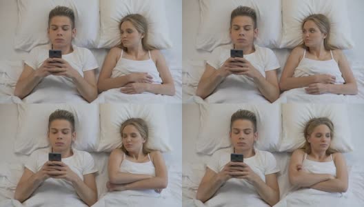 愤怒的女孩看着男友在床上用手机，网瘾高清在线视频素材下载
