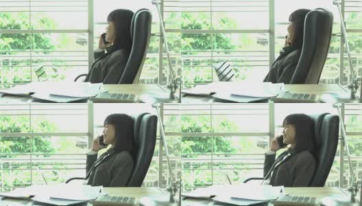概念:亚洲年轻女商务经理在家庭办公室用计算器在成堆的文件上签字之前，用智能手机说话，阅读文件报告文件高清在线视频素材下载