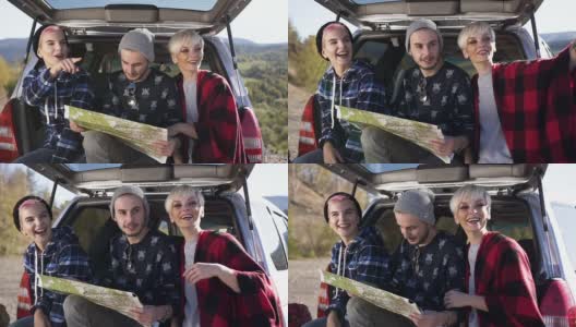 两名年轻女子和一名男子坐在汽车后备箱里用地图寻找正确的道路高清在线视频素材下载
