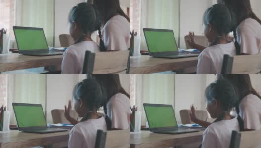 亚洲母女在家里用绿色屏幕的笔记本电脑在线视频通话问候朋友。由于Covid - 19大流行，在隔离期间儿童在家上学，父母在家工作。高清在线视频素材下载