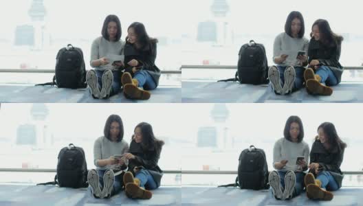 两名亚洲女性在机场候机厅使用智能手机等待航班高清在线视频素材下载