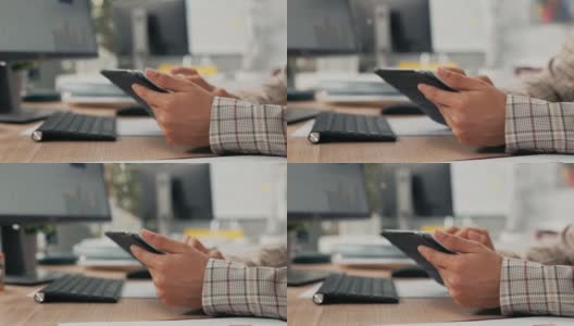这张照片拍摄的是一个女人的手拿着平板电脑，她用手指在屏幕上点击，滚动，查看电子邮件，新闻，社交媒体更新，电脑办公室，键盘在后台高清在线视频素材下载