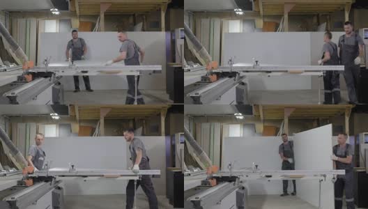 家具制造车间，两名工人正在把刨花板放到切割机上高清在线视频素材下载
