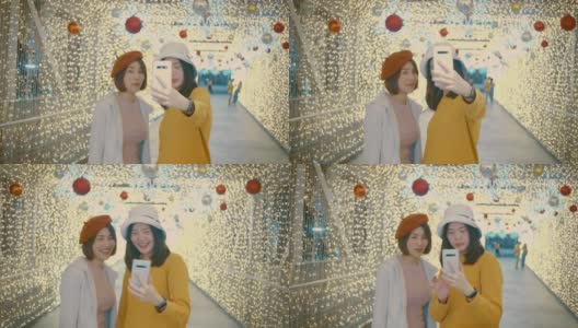 圣诞节期间，两名年轻女游客拿着装饰着彩灯的手机自拍高清在线视频素材下载