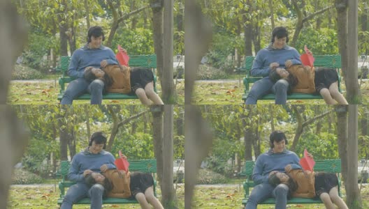 一对快乐的小情侣在公园的长椅上放松，女孩倚在男友的大腿上看书。高清在线视频素材下载