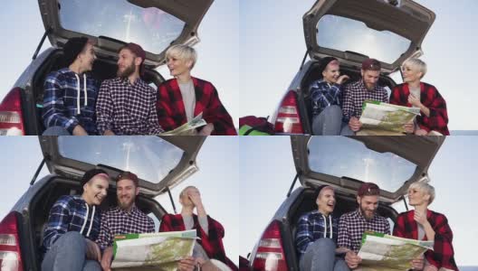 年轻的潮人朋友们坐在汽车后备箱里看地图，开心快乐。有趣的旅行和美丽的自然地点高清在线视频素材下载