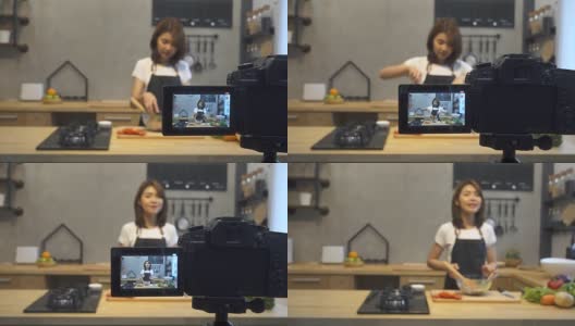 年轻的亚洲女人在厨房里给摄像机录像。微笑的亚洲女人工作的食物博主概念与水果和蔬菜在厨房。高清在线视频素材下载