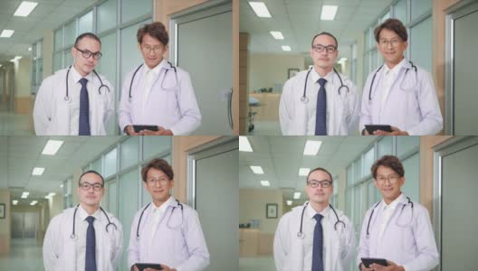 两名亚洲籍男医生，身着医务制服，站在诊所医院，面带微笑望著摄影机。高清在线视频素材下载