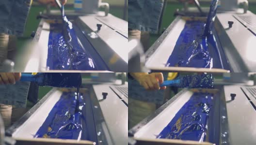 一个人在工厂印刷机的特殊装置上涂上厚厚的蓝色油漆。高清在线视频素材下载