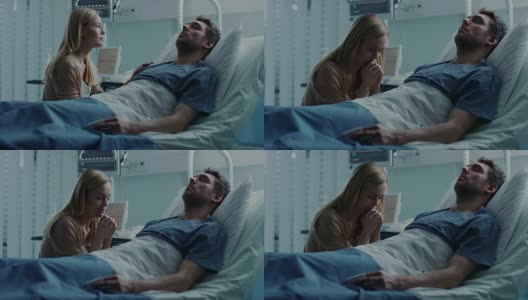 在医院里，一个病人躺在病床上，他来访的妻子满怀希望地坐在他旁边，为他的早日康复祈祷。悲惨、忧郁和忧郁的场景。高清在线视频素材下载