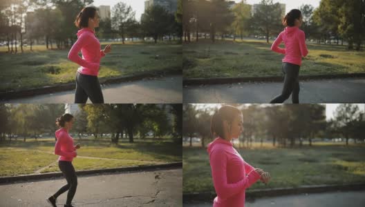 漂亮的女运动员穿着粉红色运动服在户外慢跑，健康的生活方式理念。缓慢的运动。她在用秒表计时。高清在线视频素材下载