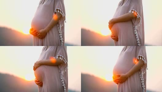 怀孕亚洲女性触摸她的腹部在粉红色的裙子与日落的背景高清在线视频素材下载
