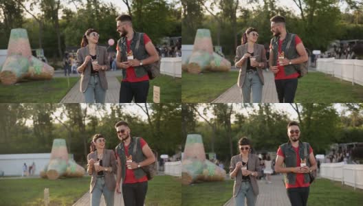 一对时髦的夫妇在城市公园散步吃着冰淇淋和华夫饼开怀大笑。浪漫的年轻男女在户外享受他们的闲暇时光。男朋友和女朋友的慢动作高清在线视频素材下载