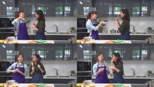 朋友们喜欢在家里做饭。亚洲妇女在家庭厨房一起做饭。两个女人在厨房跳舞。高清在线视频素材下载