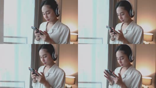 亚洲女性喜欢在家里放松的时候戴着耳机在手机上听音乐高清在线视频素材下载