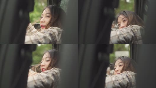 慢动作的快乐年轻美丽的亚洲女人旅行者坐在汽车与拉她的脸和手在雨天的车窗。漂亮女孩喜欢和享受户外生活方式和假期的乐趣。高清在线视频素材下载