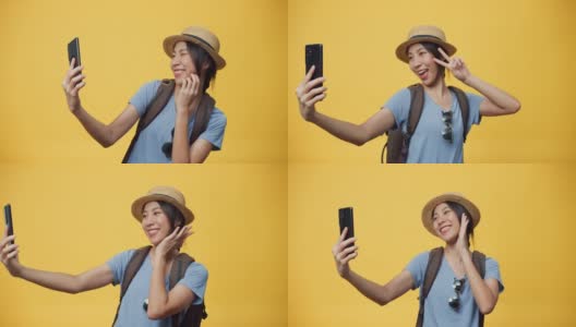 快乐青春美丽亚洲女人旅行者戴太阳镜帽子和背包微笑使用智能手机看相机拍自拍照在空白的黄色背景。高清在线视频素材下载