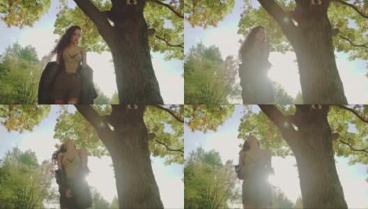 在阳光明媚的秋天，有吸引力的深色卷发女人在公园里享受时光。美丽的女人在秋天的树在户外摆姿势。风吹通风的头发在太阳在日落4k。高清在线视频素材下载