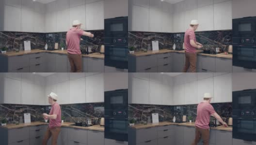 一个戴着帽子的年轻人一边做饭一边在厨房里唱歌跳舞高清在线视频素材下载