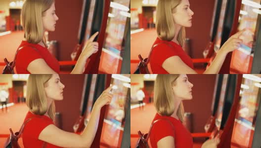 穿着红t恤的年轻漂亮女人在电影院的自动贩卖机里买电影票高清在线视频素材下载
