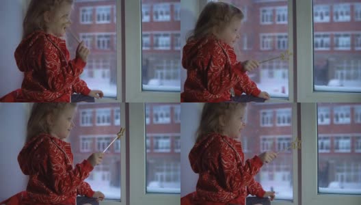 可爱的小女孩坐在窗台上，望着外面的雪景。高清在线视频素材下载