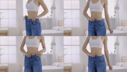 年轻苗条的女人穿着大牛仔裤在家里展示她的减肥结果高清在线视频素材下载