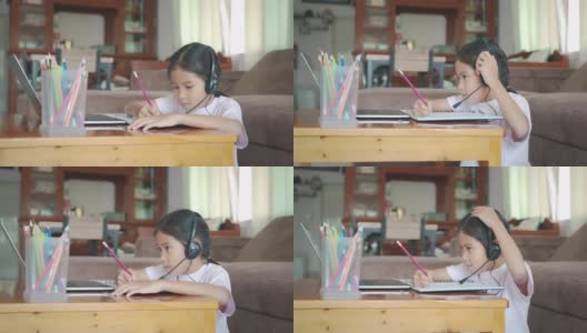 亚洲女童学生戴上耳机，通过视频电话与老师在线学习。由于Covid - 19大流行，在隔离期间，孩子正在用笔记本电脑在家学习。高清在线视频素材下载
