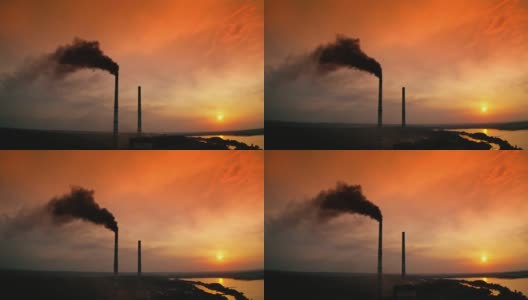 工业管道冒出的黑烟映衬着橙色的天空。日落时河边工厂烟囱的轮廓和黑烟。化学烟雾污染环境。生态灾难。高清在线视频素材下载
