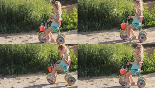 在一个阳光明媚的夏日，骑着自行车的孩子戴着太阳镜吃冰淇淋。高清在线视频素材下载