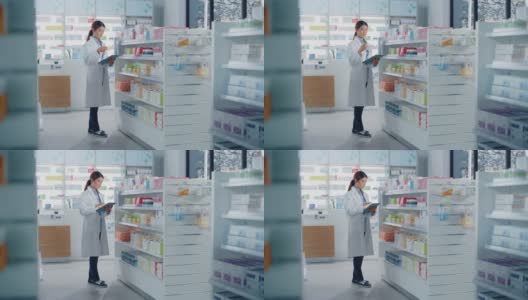 药店:美丽的亚洲药剂师使用数字平板电脑，检查库存的药物，药物，维生素，保健产品的货架上。药店专业药剂师高清在线视频素材下载