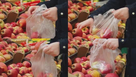 年轻女子的手把苹果放进袋子里。一位顾客正在商店里购物。高清在线视频素材下载