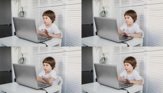 一个5岁的男孩坐在桌子旁，用笔记本电脑，看着屏幕。孩子在做作业，玩电子游戏，学习IT开发，看动画片。家庭远程在线教育理念高清在线视频素材下载