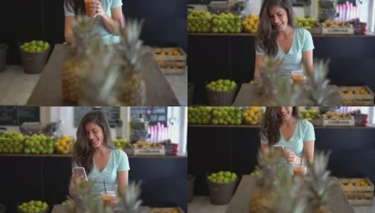 美丽的女人在一个果汁吧享受果汁，同时用她的智能手机聊天微笑高清在线视频素材下载