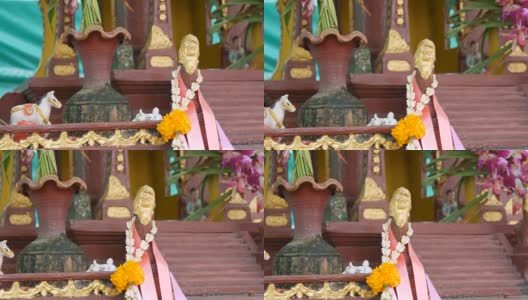 在一个花园里，棕色的佛坛供祈祷者使用，上面装饰着鲜花和各种小雕像高清在线视频素材下载