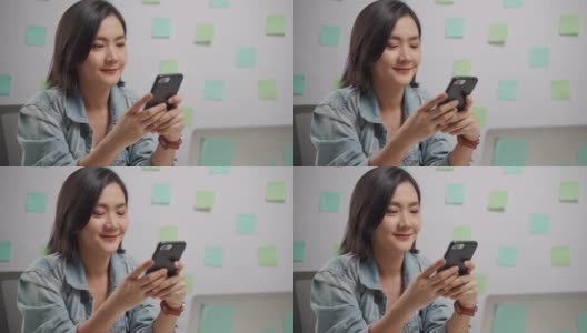 亚洲女人快乐微笑看智能手机和阅读新闻在家办公室。高清在线视频素材下载