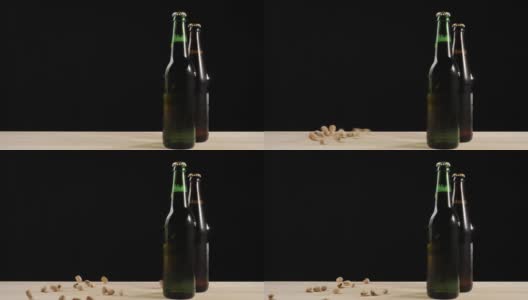 新鲜的啤酒。在黑色背景的木桌上，人们把开心果扔在绿色和棕色的瓶子旁边，还有美味的精酿啤酒。冰镇新鲜啤酒与水滴。4 k高清在线视频素材下载