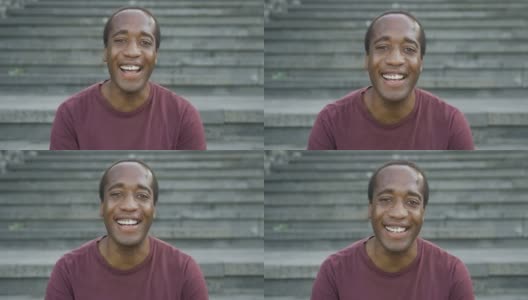 一名快乐的非洲男子坐在城市的楼梯上，对着镜头微笑高清在线视频素材下载