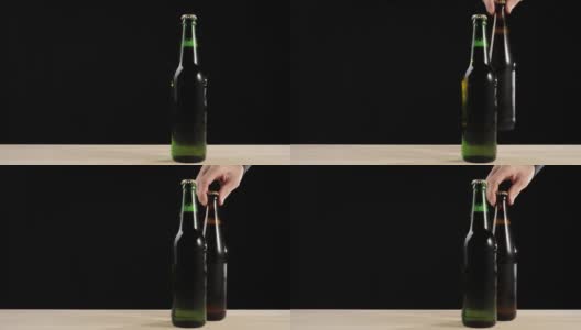 新鲜的啤酒。Hand把一个装有美味精酿啤酒的棕色瓶子和一个装有啤酒的绿色瓶子放在一张黑色背景的木桌上。冰镇新鲜啤酒与水滴。准备饮料。广角镜头。4 k高清在线视频素材下载