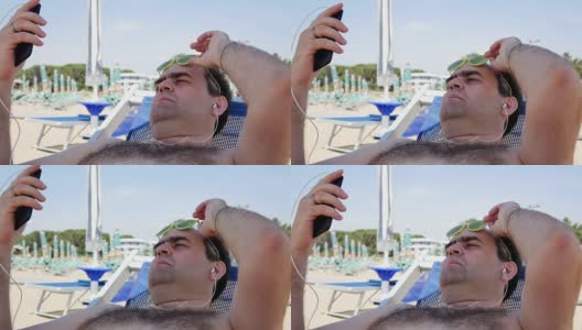 暑假，科技和人的概念-快乐的年轻人戴着太阳镜与智能手机和耳机听音乐和沙滩浴巾日光浴高清在线视频素材下载