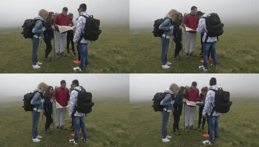 一群迷路的年轻游客徒步寻找方向，通过雾在山顶上阅读地图高清在线视频素材下载