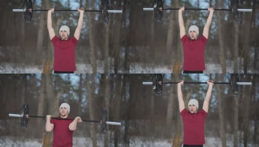 年轻肌肉发达的健美运动员站在冬天的森林里，把杠铃举过头顶高清在线视频素材下载