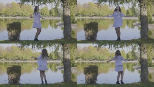 慢镜头中，一个美丽的年轻女孩穿着白色衣服，长发飘飘地在公园的湖边旋转高清在线视频素材下载